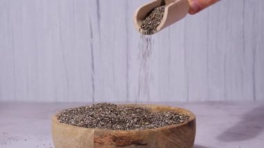 Slow motion chia seeds fall in wooden bowl. Healthy superfood rich in Omega 3 fatty acids. Dry healthy natural ingredient. Chia grains are falling. Vegetarian food 