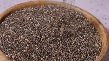 Slow motion chia seeds fall in wooden bowl. Healthy superfood rich in Omega 3 fatty acids. Dry healthy natural ingredient. Chia grains are falling. Vegetarian food 