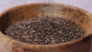 Slow motion chia seeds fall in wooden bowl. Healthy superfood rich in Omega 3 fatty acids. Dry healthy natural ingredient. Chia grains are falling. Vegetarian food 