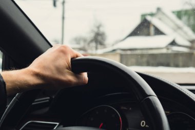 Selective focus mans hand on steering wheel, driving car in winter background. Black luxury modern car Interior. Steering wheel, shift lever and dashboard. Black leather Detail Automatic gear stick