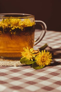 Dandelion flower healthy tea in glass cup on table. Herbal medicine Delicious tisane tea from with fresh yellow blossom dandelion flowers inside tea cup. Green clearing infusion Wildflowers Eco