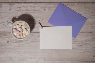 Empty greeting or invitation card mock up violet envelope with white cup of coffee and marshmallows on wooden blue background. Blank paper copy space for your text. Valentines day, Happy fathers