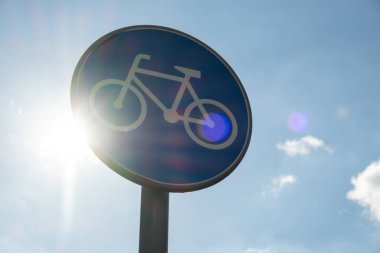 Round road sign depicting white bicycle on blue background, meaning mandatory bike path for cyclists against blue sky background. Blue round sign on bike path pole. Bike path