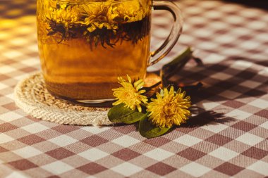Dandelion flower healthy tea in glass cup on table. Herbal medicine Delicious tisane tea from with fresh yellow blossom dandelion flowers inside tea cup. Green clearing infusion Wildflowers Eco
