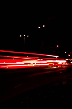 Geceleri arabaların ışıkları. Sokak lambaları. Gece Karayolu Şehri. Uzun pozlu fotoğraf gece yolu. Yoldaki renkli kırmızı ışık şeritleri. Arkaplan duvar kağıdı bulanık fotoğrafa odaklanmış