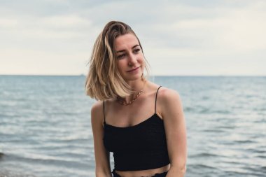 Young woman standing on blurred beachside background. Attractive female enjoying walking the sea shore. travel and active lifestyle concept. Springtime. Relaxation, youth, love, lifestyle solitude