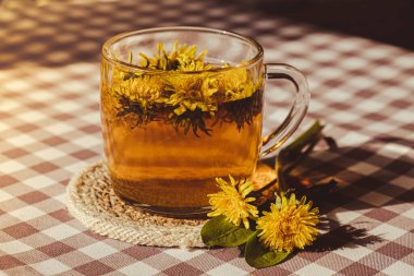 Dandelion flower healthy tea in glass cup on table. Herbal medicine Delicious tisane tea from with fresh yellow blossom dandelion flowers inside tea cup. Green clearing infusion Wildflowers Eco