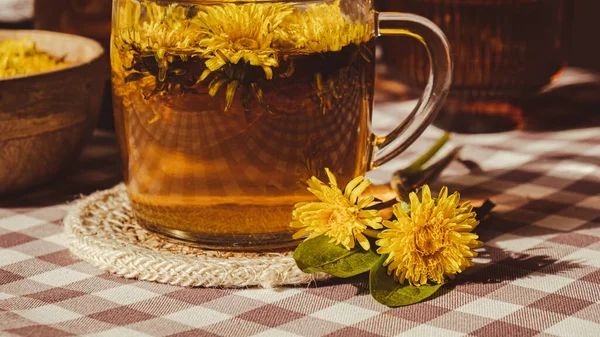 Stock image Dandelion flower healthy tea in glass cup on table. Herbal medicine Delicious tisane tea from with fresh yellow blossom dandelion flowers inside tea cup. Green clearing infusion Wildflowers Eco