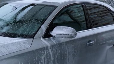 Washing luxury silver car on touchless car wash. Washing sedan car with foam self-service and high pressure water. Winter cleaning in car wash. Cleanliness and order in urban environment