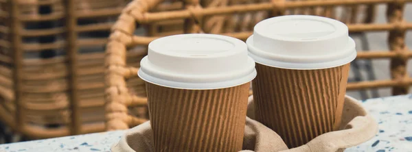 Two paper cups with lid for tea to go. Coffee take away on the table. Take-out coffees with brown paper cup holder. Brown safety cardboard collars. Take away box for cups. Cardboard tray