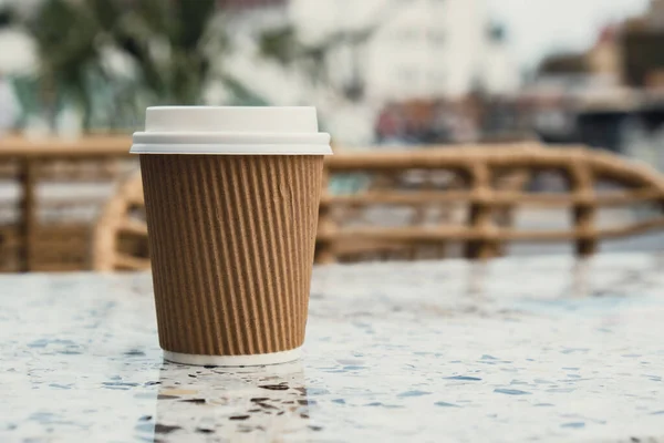 Eco recycling paper cup with coffee or tea on craft paper on table in beach cafe. Take away coffee to go. Copy space for text. Disposable Cardboard coffee outdoors