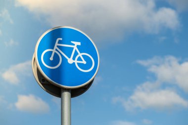 Round road sign depicting white bicycle on blue background, meaning mandatory bike path for cyclists against blue sky background. Blue round sign on bike path pole. Bike path