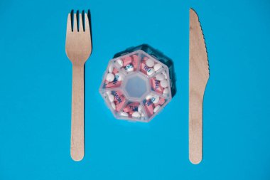 Organizer weekly shots with fork and knife medical pill box with doses of tablets for daily take medicine with white pink drugs and capsules. Daily vitamins at home. Medication dietary supplements