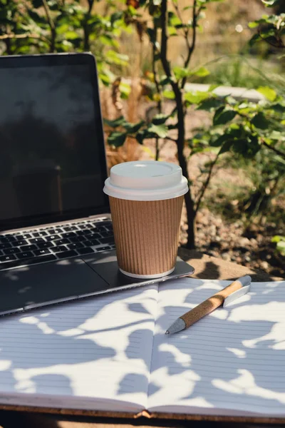 Take away coffee in craft recycling paper cup with paper notebook and laptop. Freelancers place of work. Study and work online. Remote business education. View webinar. E-learning Workstation on