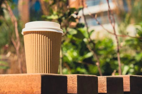 Eco recycling paper cup with coffee or tea on kraft paper on wooden table. Breakfast on the street in the park on bench. Take away coffee to go. Copy space for text. Disposable Cardboard coffee