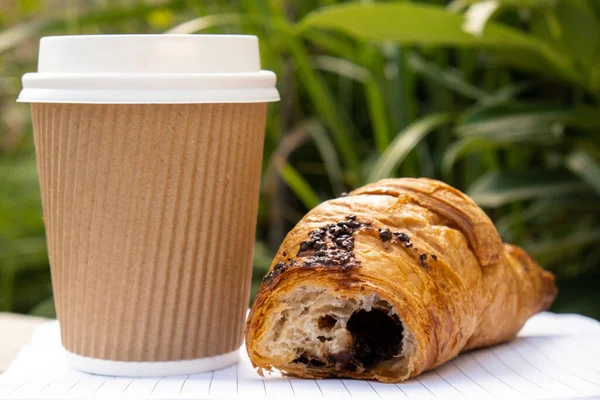 Fresh baked chocolate croissant on paper cup with lid for tea to go. Empty paper notebook. Freelancers place of work. Study and work online. Remote business education. Making plans for next week year