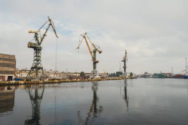 Motlawa river to Baltic Sea. Coal mine, polluting environment by the river POV from ferry swimming on river canal. Industrial building at the Gdansk Shipyard. Prefabrication workshop and heavy cranes