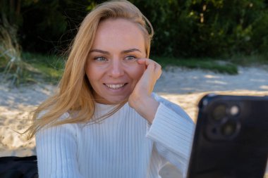 Portrait of Happy young woman take selfie on the beach sea ocean. Smiling to camera while making video call. Influencer and content creator on social media. Leisure in nature. Wellbeing unity with