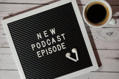 Tahta masada üzerinde yeni PODCAST EPISODE yazılı beyaz kahve fincanı kablosuz kulaklıkla duyuru panosu. Podcast konsepti. Radyodaki ses iyileştirme sağlık alışkanlıkları.