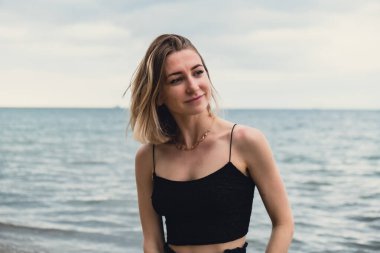 Young woman standing on blurred beachside background. Attractive female enjoying walking the sea shore. travel and active lifestyle concept. Springtime. Relaxation, youth, love, lifestyle solitude