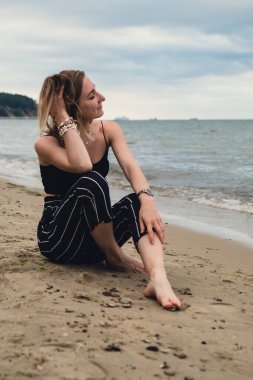 Young woman siting on blurred beachside background. Attractive female enjoying the sea shore. travel and active lifestyle concept. Springtime. Relaxation, youth, love, lifestyle solitude with nature