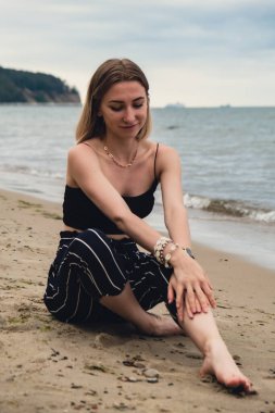 Young woman siting on blurred beachside background. Attractive female enjoying the sea shore. travel and active lifestyle concept. Springtime. Relaxation, youth, love, lifestyle solitude with nature