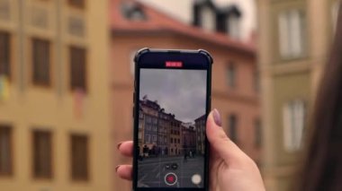 Female traveler in historical places looks around courtyard of landmark and shoots short video on phone. Tourist photographs historic place on sunny day. Unrecognizable woman Tourism and blogging