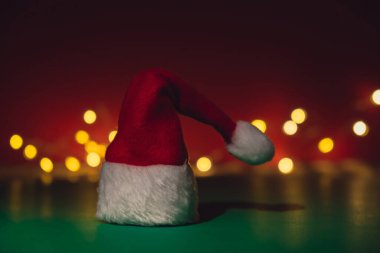 Santa hat on isometric green red background. Defocused lights on backdrop Copy space for your text. Mock up for advertisement. Holiday Christmas composition. Minimalistic greeting card. Creative 