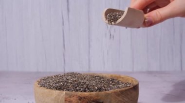Slow motion chia seeds fall in wooden bowl. Healthy superfood rich in Omega 3 fatty acids. Dry healthy natural ingredient. Chia grains are falling. Vegetarian food 