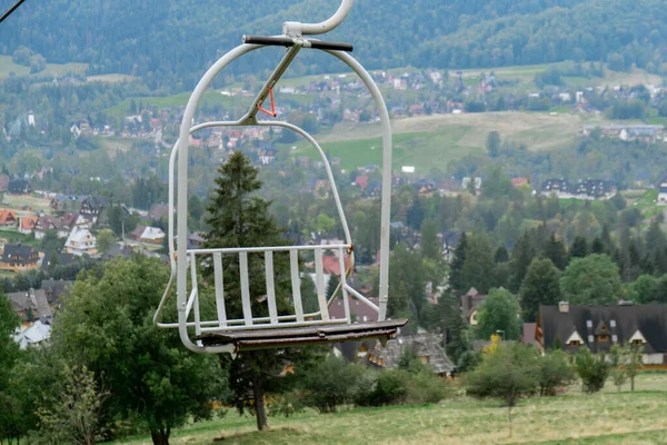 スキーリフト椅子リフトで雪の山の秋の森ザコパネポーランドのスキーリゾートで 休日休暇スポーツやアウトドア活動観光ケーブルカー緑の森の中の空のシート草のフィールド — ストック写真
