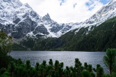 Morskie Oko lake Snowy Mountain Hut in Polish Tatry mountains, Zakopane, Poland. Beautiful green hills and mountains in dark clouds and reflection on the lake Morskie Oko lake. Travel tourist
