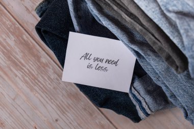 ALL YOU NEED IS LESS text on paper note on Jeans clothes assortment Second hand sustainable shopping. Capsule minimal wardrobe. Sustainable fashion overconsumption, conscious buying consumption, slow clipart