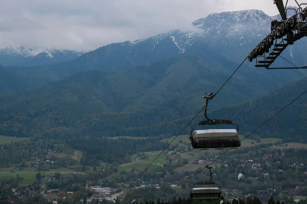 スキーリフト椅子リフトで雪の山の秋の森ザコパネポーランドのスキーリゾートで 休日休暇スポーツやアウトドア活動観光ケーブルカー緑の森の中の空のシート草のフィールド — ストック写真