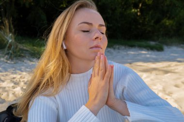 Genç bir kadın deniz kıyısında meditasyon yapıyor. Nefes almak zihinsel sağlığa iyi gelir. Nefes terapisi. Kundalini enerjisini her gün dengelemek kadın sağlığına iyi gelir.