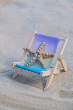 Sunny holidays on the beach with sand beach accessories with sea shells and sea star. Sun lounger stand sea Ocean background. Wooden beach chairs. Summer holiday vacation concept. 