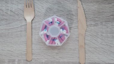 Organizatör haftalık çekimlerini çatal ve bıçak ilaç kutusuyla yakınlaştır günlük dozda tablet beyaz pembe ilaç ve kapsüllerle ilaç al. Evde günlük vitaminler. İlaç diyeti
