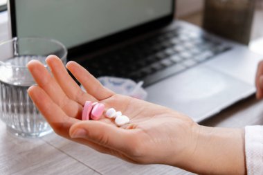 Woman taking Daily vitamins white working on laptop Organizer weekly shots Closeup of medical pill box with doses of tablets for daily take medicine with white pink drugs and capsules. Workplace