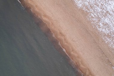 Winter in cold Baltic sea snowy beach in Gdansk. Aerial view of snow covered beach and dunes and dark calm sea nature landscape captured with drone. Winter tourism in Poland