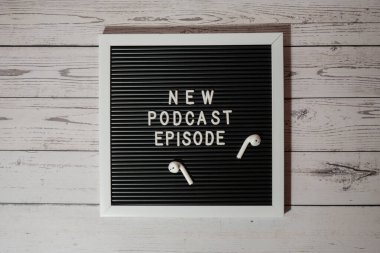 Yeni PODCAST EPISODE yazılı duyuru panosu ahşap masada kablosuz kulaklıklarla. Podcast konsepti. Radyodaki ses iyileştirme sağlık alışkanlıkları.