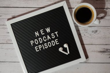 Tahta masada üzerinde yeni PODCAST EPISODE yazılı beyaz kahve fincanı kablosuz kulaklıkla duyuru panosu. Podcast konsepti. Radyodaki ses iyileştirme sağlık alışkanlıkları.