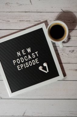 Tahta masada üzerinde yeni PODCAST EPISODE yazılı beyaz kahve fincanı kablosuz kulaklıkla duyuru panosu. Podcast konsepti. Radyodaki ses iyileştirme sağlık alışkanlıkları.