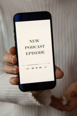 Elinde cep telefonu olan tanınmayan bir kadın. YENİ PODCAST EPISODE. Kablosuz kulaklıklı web sitesi uygulaması. Ses iyileştirme, ses terapisi sağlık ritüelleri, pozitif ruh sağlığı.