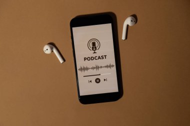 Kablosuz kulaklıklar ve cep telefonu Podcast dinleme sitesi uygulaması bej arka planda. Ses iyileştirme, ses terapisi sağlık ritüelleri, olumlu ruh sağlığı alışkanlıkları. Millenial Blogger