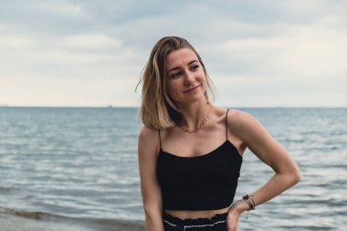 Young woman standing on blurred beachside background. Attractive female enjoying walking the sea shore. travel and active lifestyle concept. Springtime. Relaxation, youth, love, lifestyle solitude