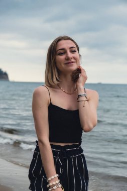 Young woman standing on blurred beachside background. Attractive female enjoying walking the sea shore. travel and active lifestyle concept. Springtime. Relaxation, youth, love, lifestyle solitude