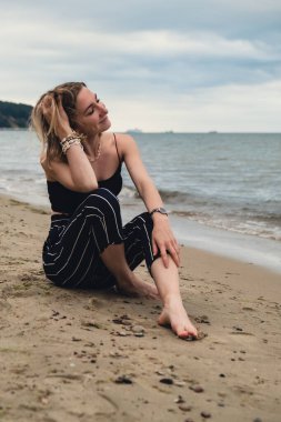 Young woman siting on blurred beachside background. Attractive female enjoying the sea shore. travel and active lifestyle concept. Springtime. Relaxation, youth, love, lifestyle solitude with nature