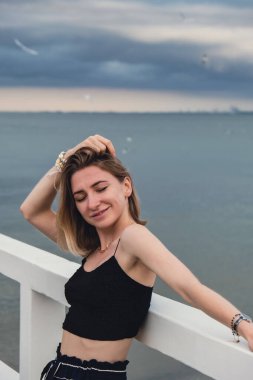 Young woman standing on wooden pier blurred beachside background. Attractive female enjoying the sea shore travel and active lifestyle concept. Springtime. Wellness wellbeing mental health inner peace