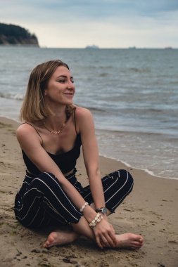 Young woman siting on blurred beachside background. Attractive female enjoying the sea shore. travel and active lifestyle concept. Springtime. Relaxation, youth, love, lifestyle solitude with nature