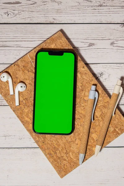 Top view, wooden Office desk mobile phone chroma key screen mock up mobile app application eco pen, wireless headphones and recycle notebook. Business or student workspace concept Flat lay. Modern