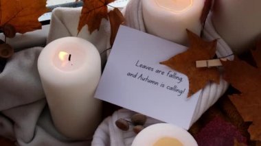 Yapraklar Düşüyor ve AUTUMN, örgü örülmüş sonbahar yaprakları, baharatlar ve mum eşliğinde Hygge 'nin pencere kenarındaki evinde sonbahar tatilini kutlayan metin tebrik kartı konseptini arıyor.